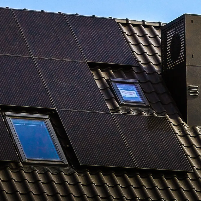 Ein dunkles Ziegeldach, auf dem schwarze Solarpaneele montiert sind. Daneben Schornsteine.