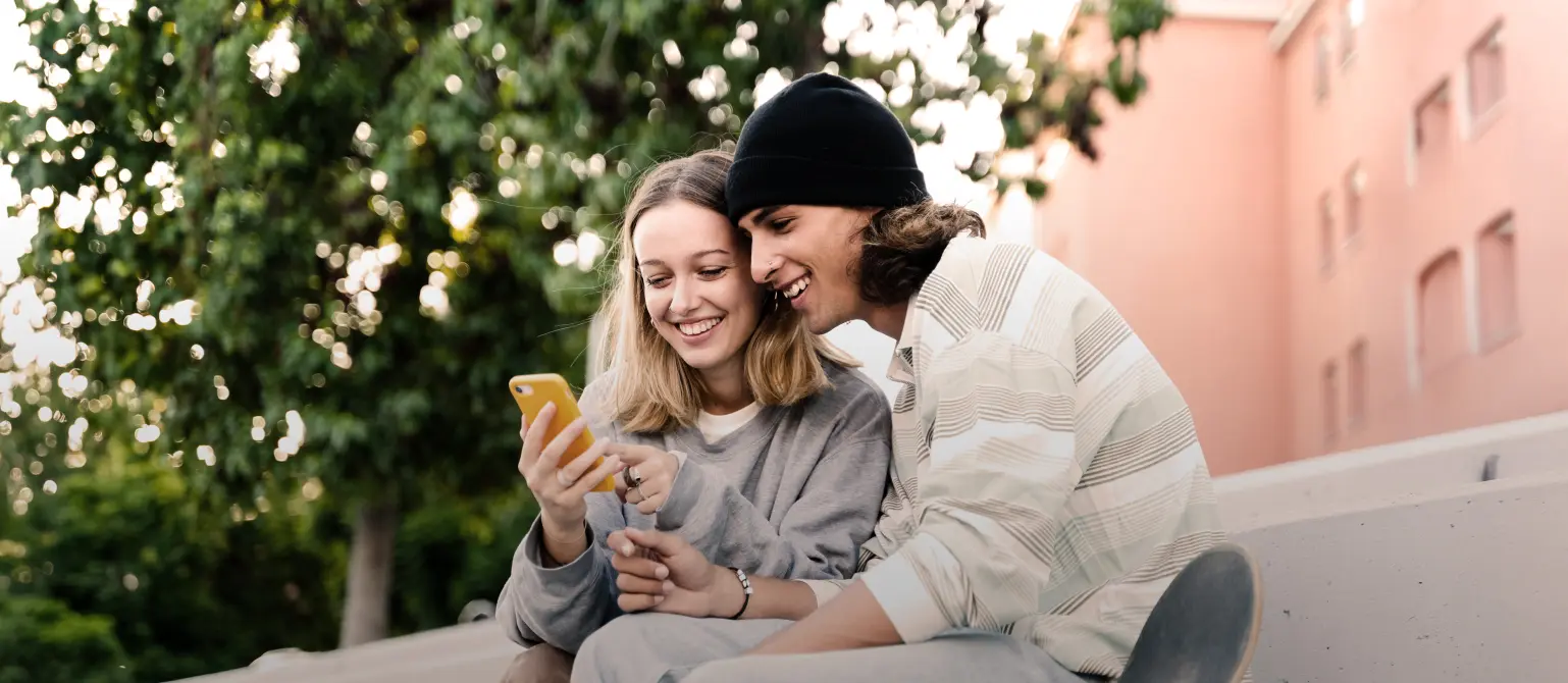 Eine Frau und ein Mann sitzen nebeneinander und schauen gemeinsam lachend auf ein Handy