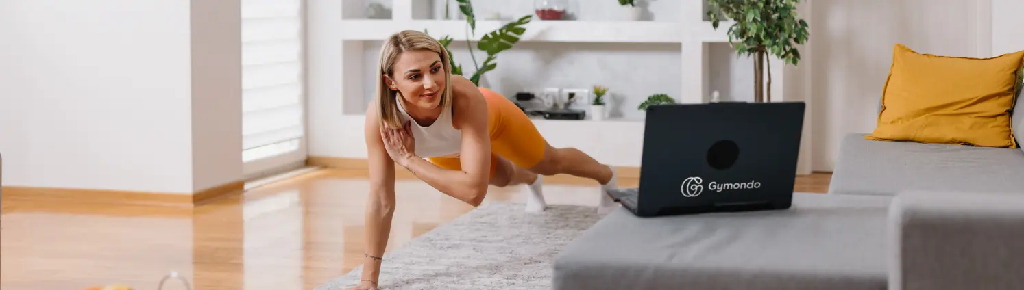Yoga: Eine Frau in Sportkleidung macht ein Home-Workout vor ihrem Laptop im Wohnzimmer.