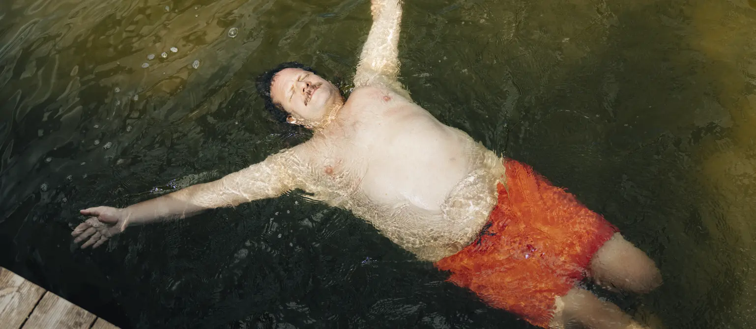 Ein kräftiger Mann lässt sich im Wasser treiben und trägt eine knallige Badehose
