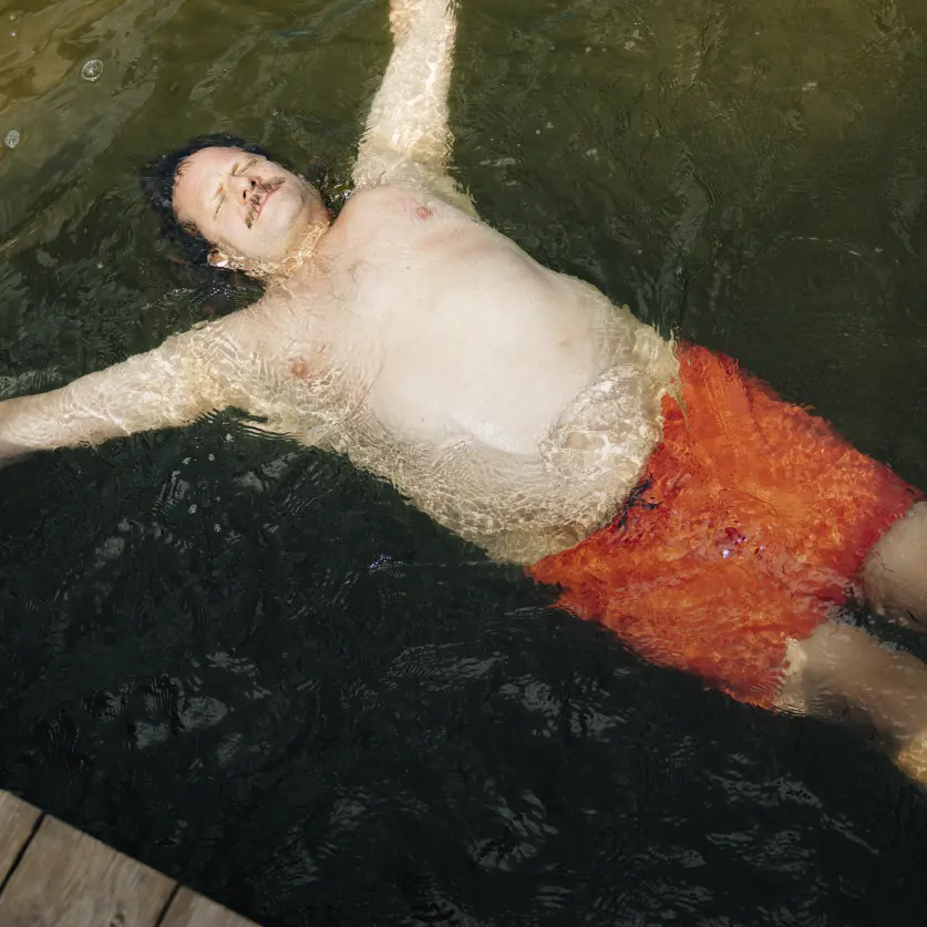 Ein kräftiger Mann lässt sich im Wasser treiben und trägt eine knallige Badehose