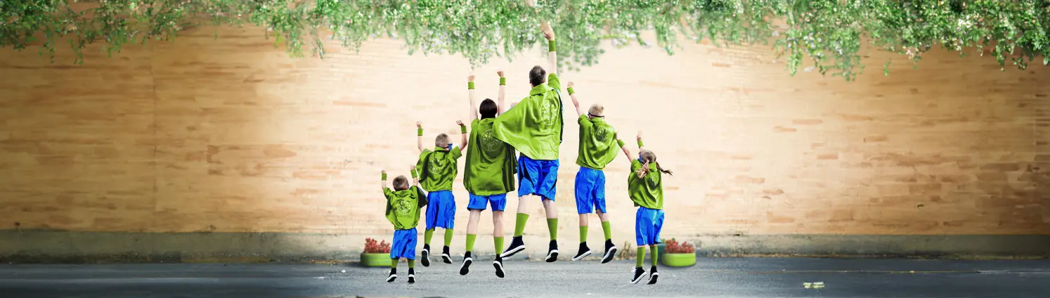 Familie, die als Superhelden in grün-blau gekleidet, sind von hinten zu sehen und machen eine Superman-Pose.