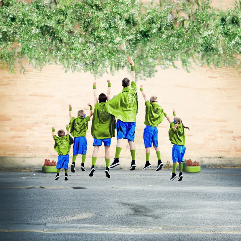 Familie, die als Superhelden in grün-blau gekleidet, sind von hinten zu sehen und machen eine Superman-Pose.