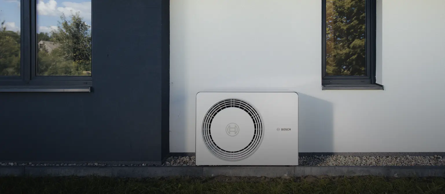 Eine Wärmepumpe von Energie Brandenburg steht vor der Wand eines Einfamilienhauses, umgeben von Garten.
