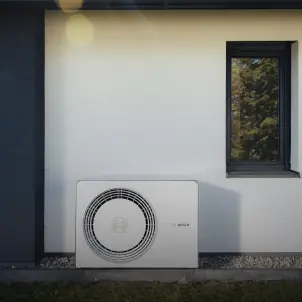 Eine Wärmepumpe von Energie Brandenburg steht vor der Wand eines Einfamilienhauses, umgeben von Garten.