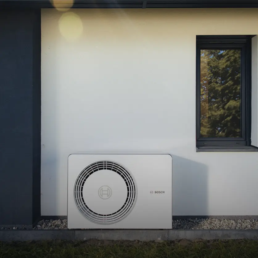 Eine Wärmepumpe von Energie Brandenburg steht vor der Wand eines Einfamilienhauses, umgeben von Garten.