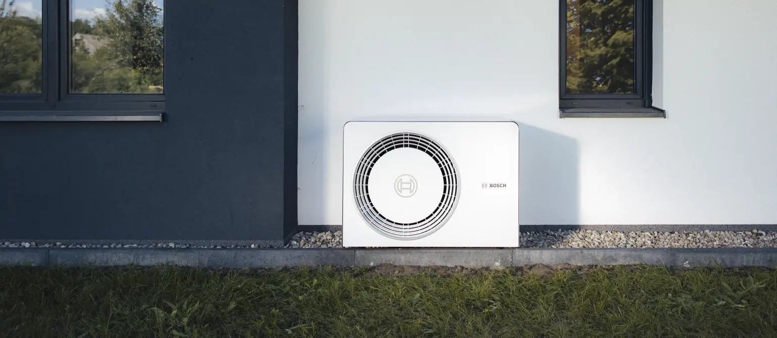 Eine weiße Wärmepumpe steht im Garten vor einem Haus