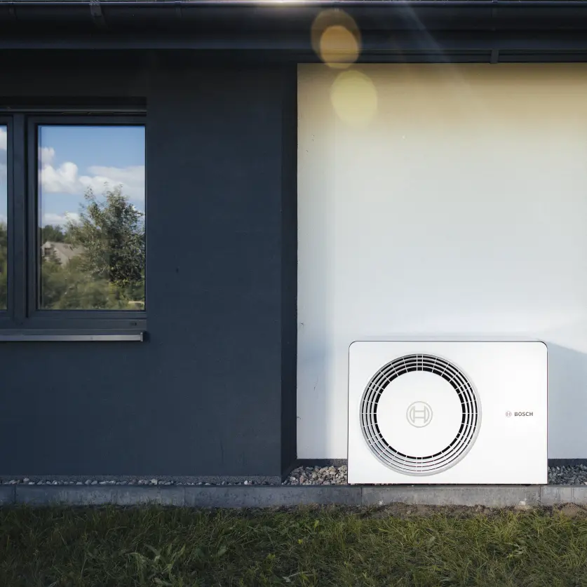 Eine weiße Wärmepumpe steht im Garten vor einem Haus