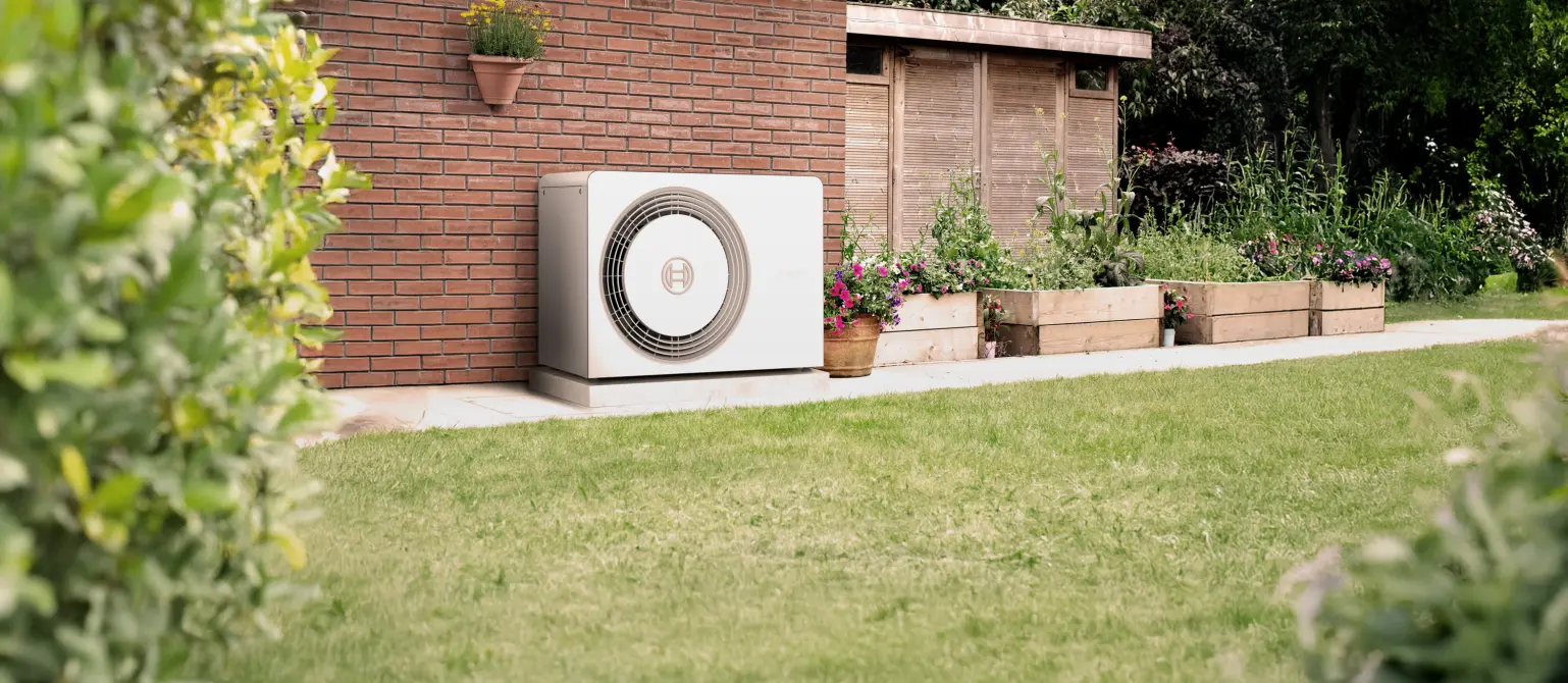 Eine Wärmepumpe steht im Garten vor einer Hauswand