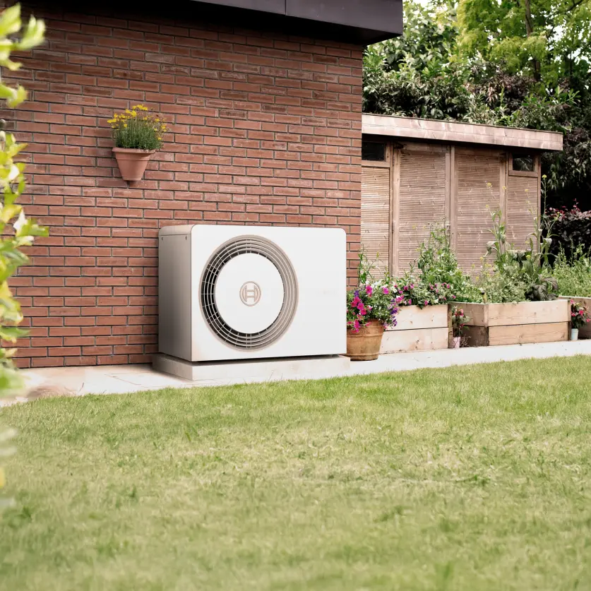 Eine Wärmepumpe steht im Garten vor einer Hauswand 