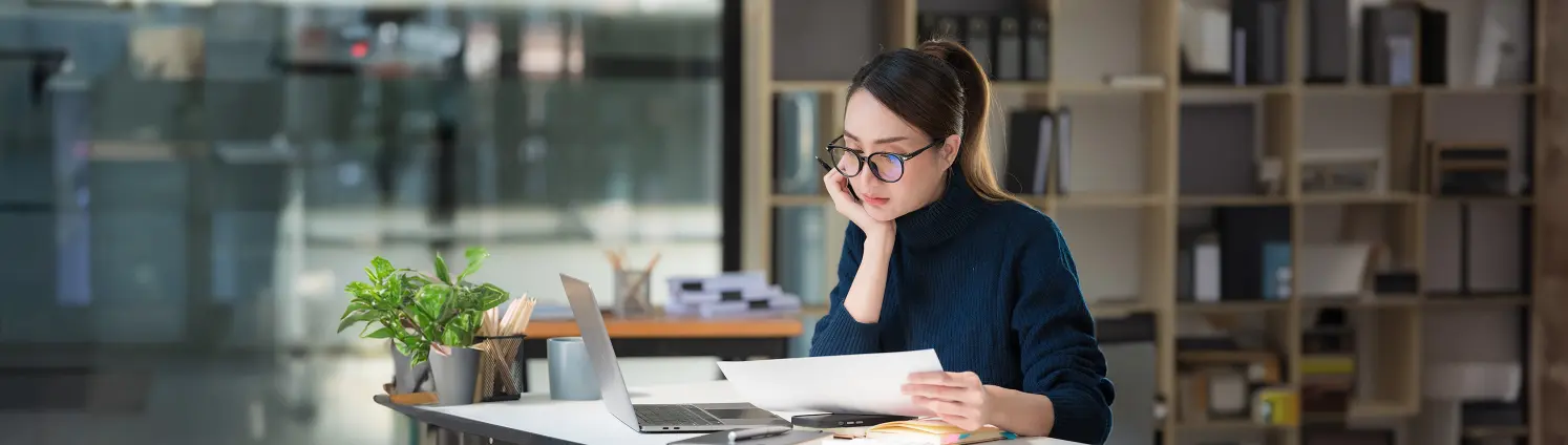 Eine Frau mit Brille sitzt am Schreibtisch und studiert Aufzeichnungen.