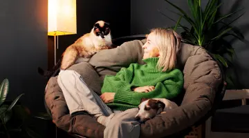 Eine Frau sitzt auf einem Sessel, links daneben sitzt eine Katze auf der Armlehne