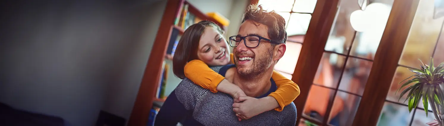 Kind umarmt seinen lachenden Vater von hinten.