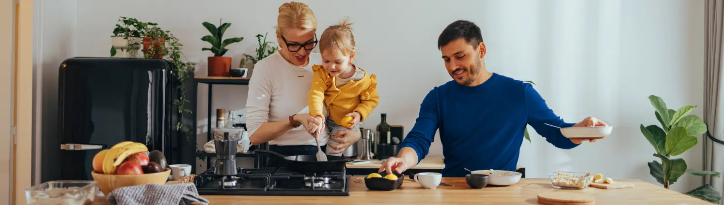 Vater, Mutter und Kleinkind kochen gemeinsam in der Küche am Gasherd.