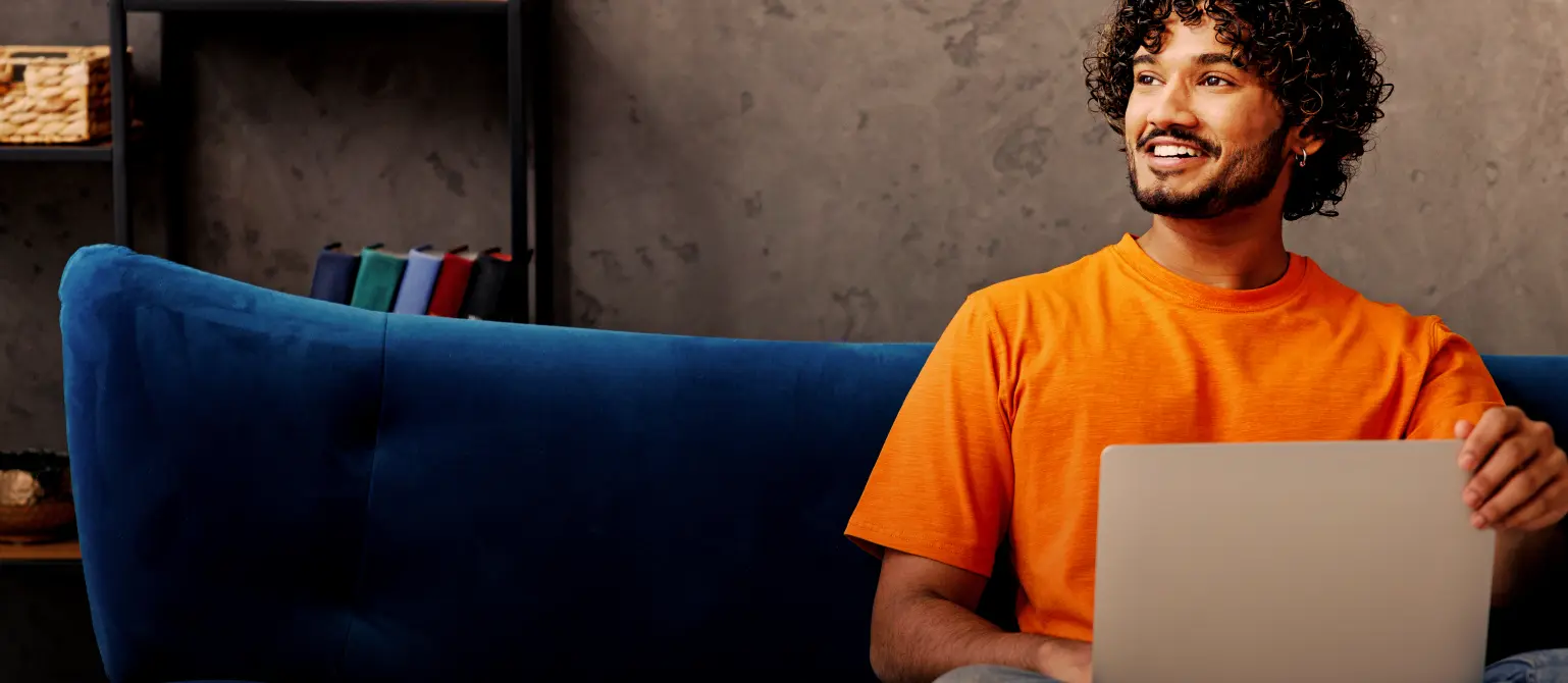 Ein Mann sitzt auf seinem blauen Sofa und recherchiert etwas am Laptop