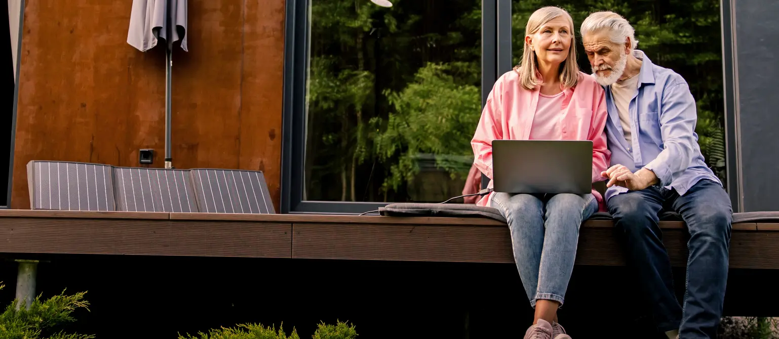 Ein älteres Ehepaar sitzt auf der Terrasse und schaut auf einen Laptop