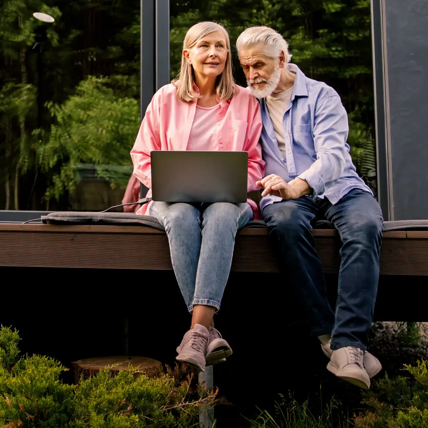 Ein älteres Ehepaar sitzt auf der Terrasse und schaut auf einen Laptop