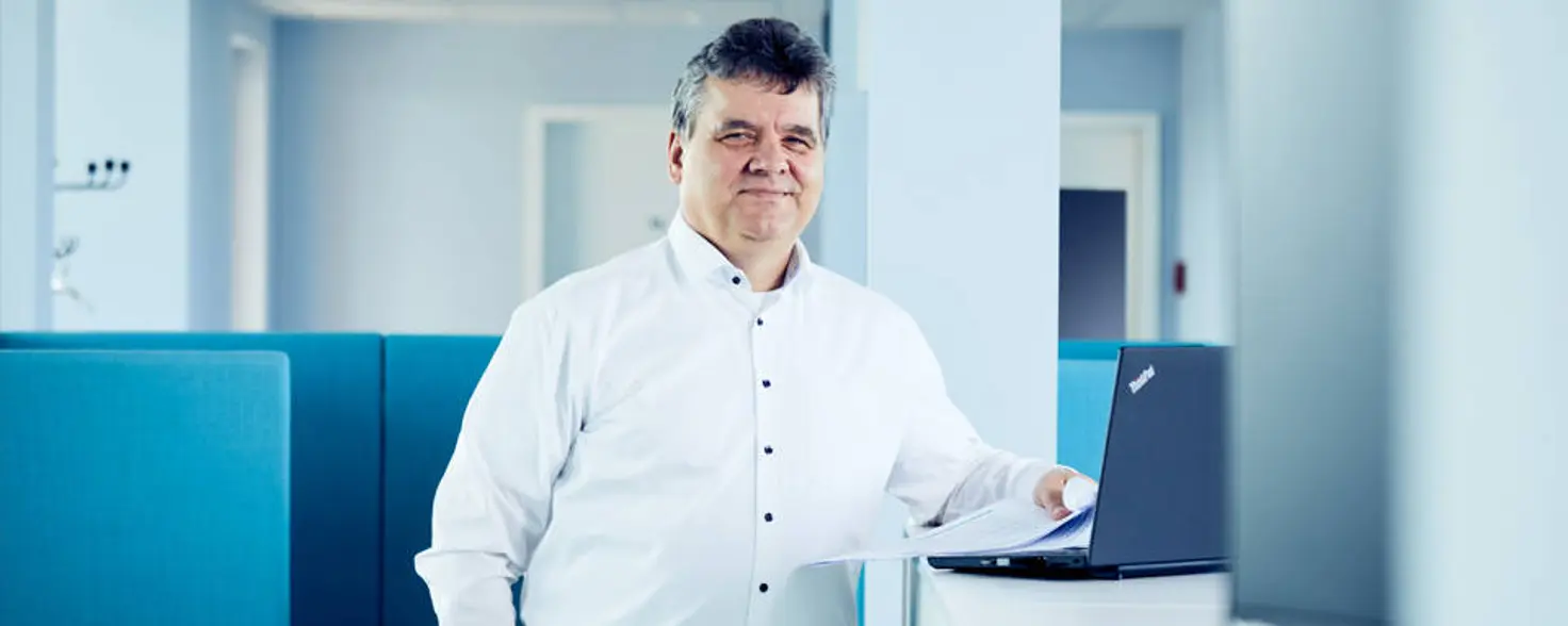 Geschäftsführer Dr. Jens Horn steht neben einem Laptop und schaut in die Kamera.