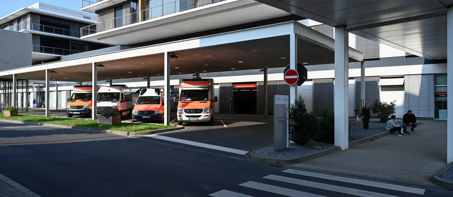 Vier Krankenwagen stehen vor einem modernen Krankenhaus unter einer Bedachung.