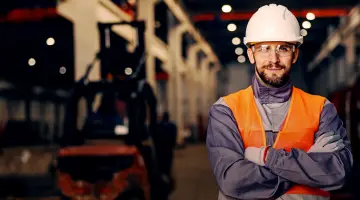 Ein Mann mit Helm, Schutzbrille und Arbeitsweste schaut in die Kamera