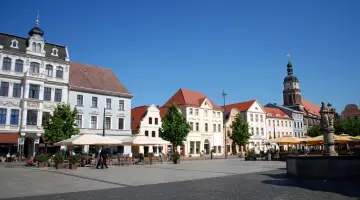 Der Marktplatz in Cottbus mit einem Springbrunnen in der Mitte und drumherum mehrstöckige Häuser.
