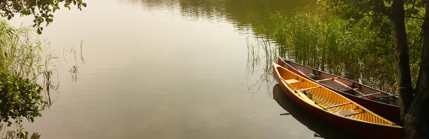 Ein Brandenburger See in bewaldeter Umgebung, am Ufer sind zwei Kanus angeleint.
