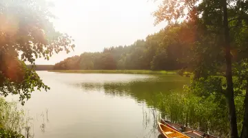 Ein Brandenburger See in bewaldeter Umgebung, am Ufer sind zwei Kanus angeleint.