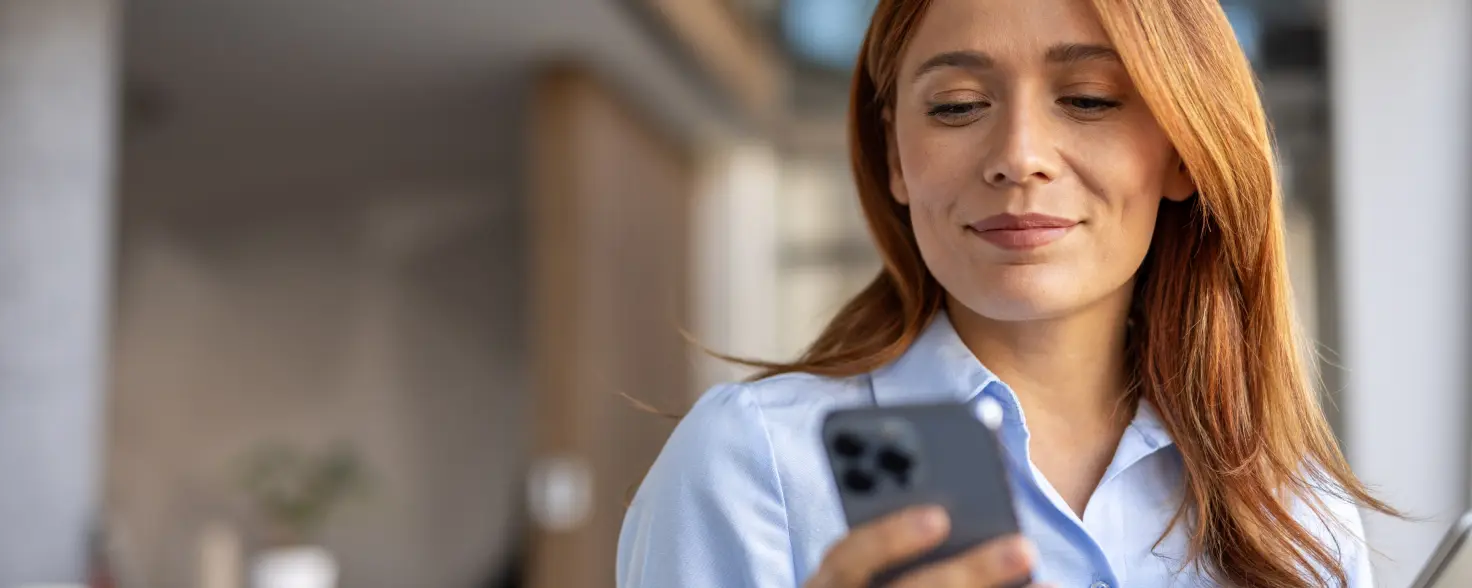 Eine junge Frau mit roten Haaren schaut auf ihr Smartphone.