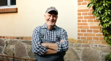 Handwerker schaut freundlich in die Kamera in einem karierten Hemd und Arbeitshose