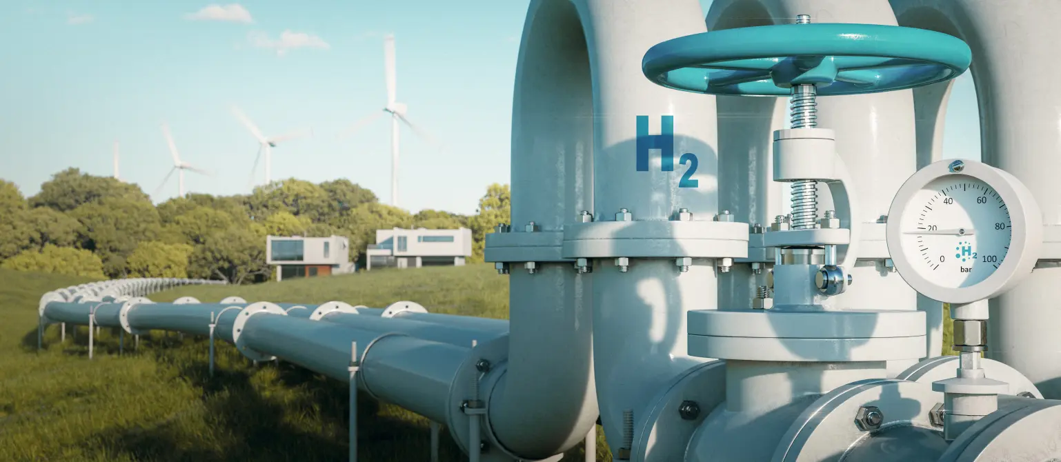 Eine Wasserstoffpipeline führt über eine grüne Wiese zu modernen Einfamilienhäusern. Im Hintergrund Windkraftanlagen.