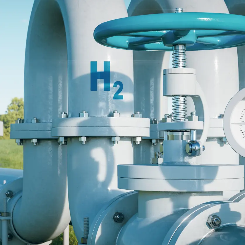Eine Wasserstoffpipeline führt über eine grüne Wiese zu modernen Einfamilienhäusern. Im Hintergrund Windkraftanlagen.