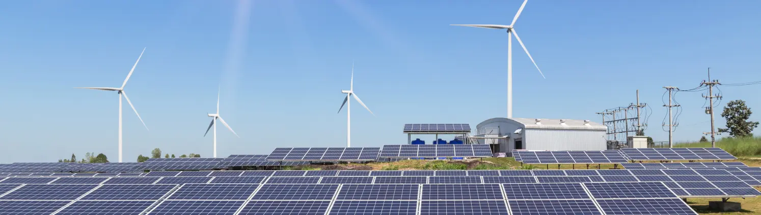 Im Vordergrund ein Feld von Solarzellen vor mehreren Windkraftanlagen, die in den blauen Sommerhimmel ragen.