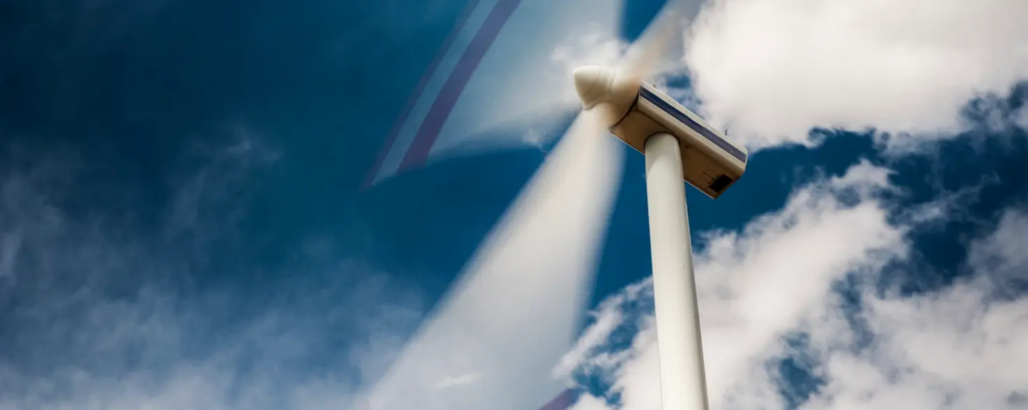 Der Rotor einer Windkraftanlage dreht sich vor blauem Himmel mit Schönwetterwolken.