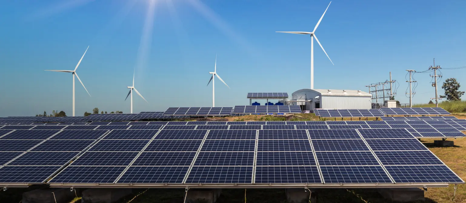 Im Vordergrund ein Feld von Solarzellen vor mehreren Windkraftanlagen, die in den blauen Sommerhimmel ragen.
