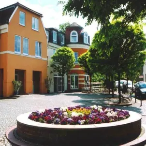 Das orangerote Rathaus der Gemeinde Schwielowsee im Kreis Potsdam-Mittelmark. Davor ein blühendes Rundbeet.