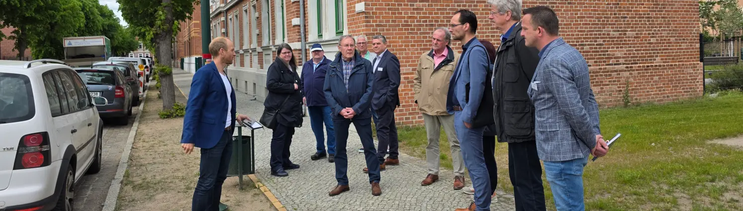 Kommunaler Stammtisch von Energie Brandenburg in Falkenberg/Elster: Bürgermeister Stephan Bawey führt eine Gruppe durch eine Straße mit Altbauten.