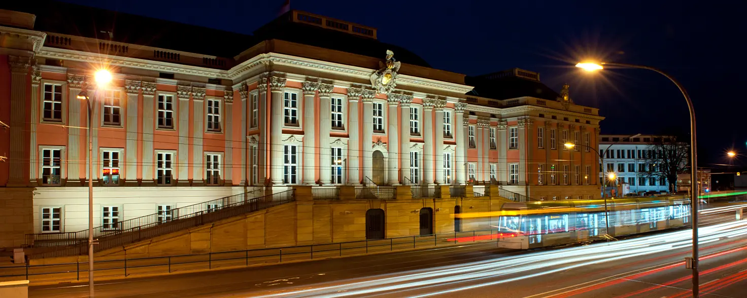 Rathaus der brandenburgischen Landeshauptstadt Potsdam bei Nacht. Davor eine breite Straße mit Lichteffekten.