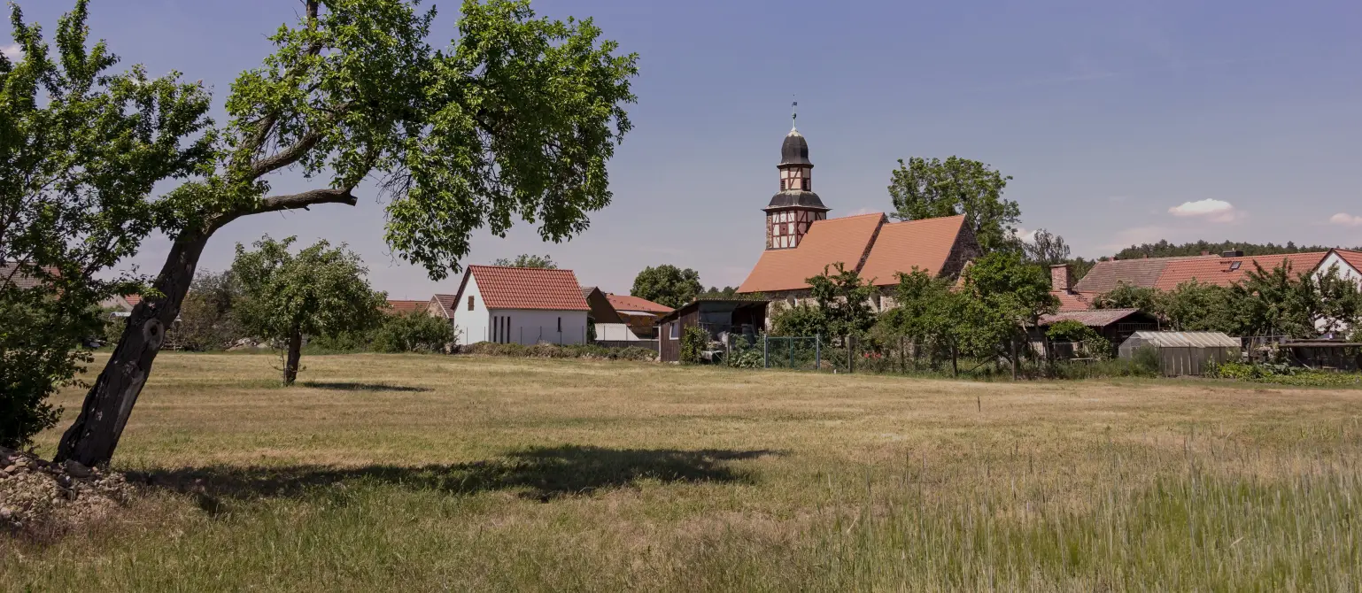 Blick über Wiesen und Felder auf die Fachwerkkirche im Dorf Raben im Hohen Fläming im Land Brandenburg.