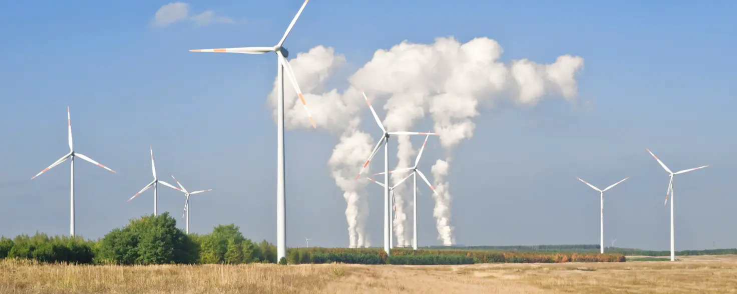 Windkraft in der Lausitz: Windräder auf offenem Feld vor Kohlekraftwerk mit aufsteigendem Dampf unter blauem Himmel.