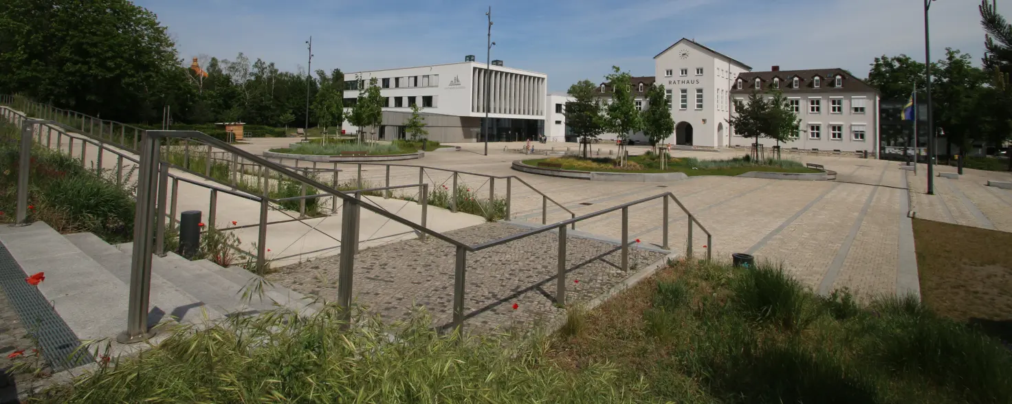 Rathaus von Hohen Neuendorf mit modernem Vorplatz, Treppen und Grünflächen unter blauem Himmel.