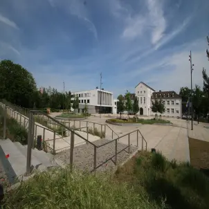 Rathaus von Hohen Neuendorf mit modernem Vorplatz, Treppen und Grünflächen unter blauem Himmel.