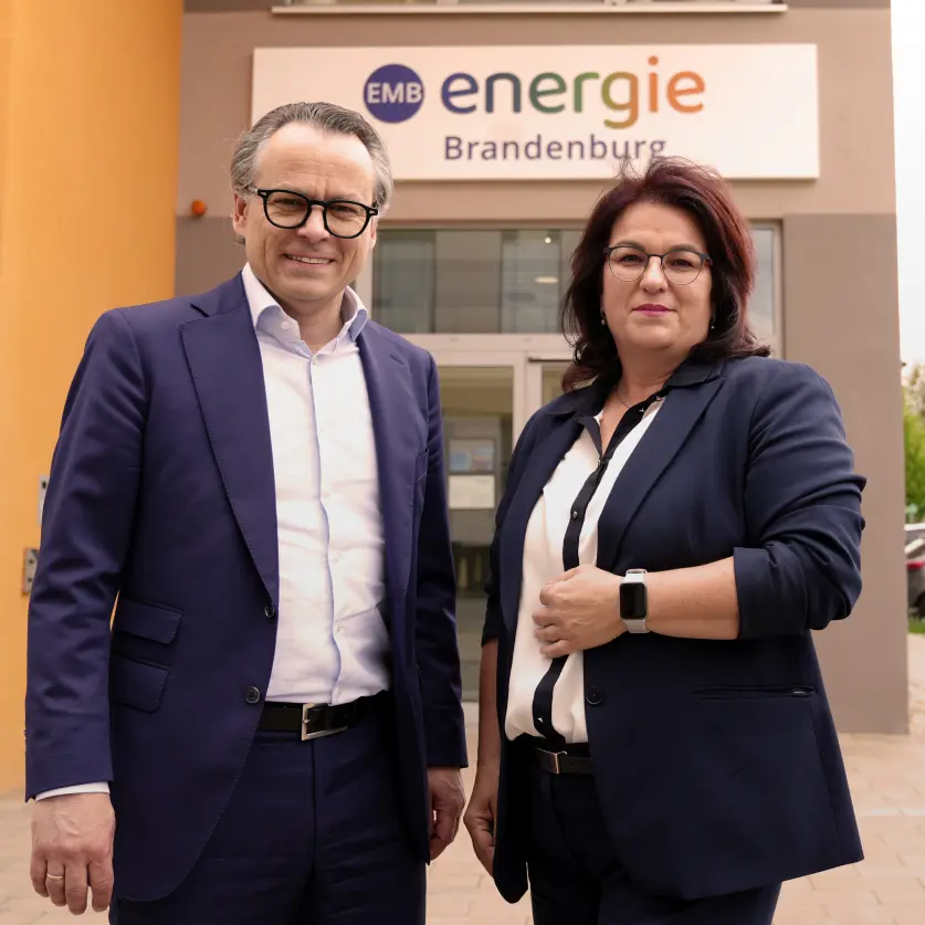 Leif Christian Cropp und Kathrin Jung: Zwei Personen in Businesskleidung stehen vor dem Eingangsbereich eines Gebäudes mit Energie Brandenburg-Logo.