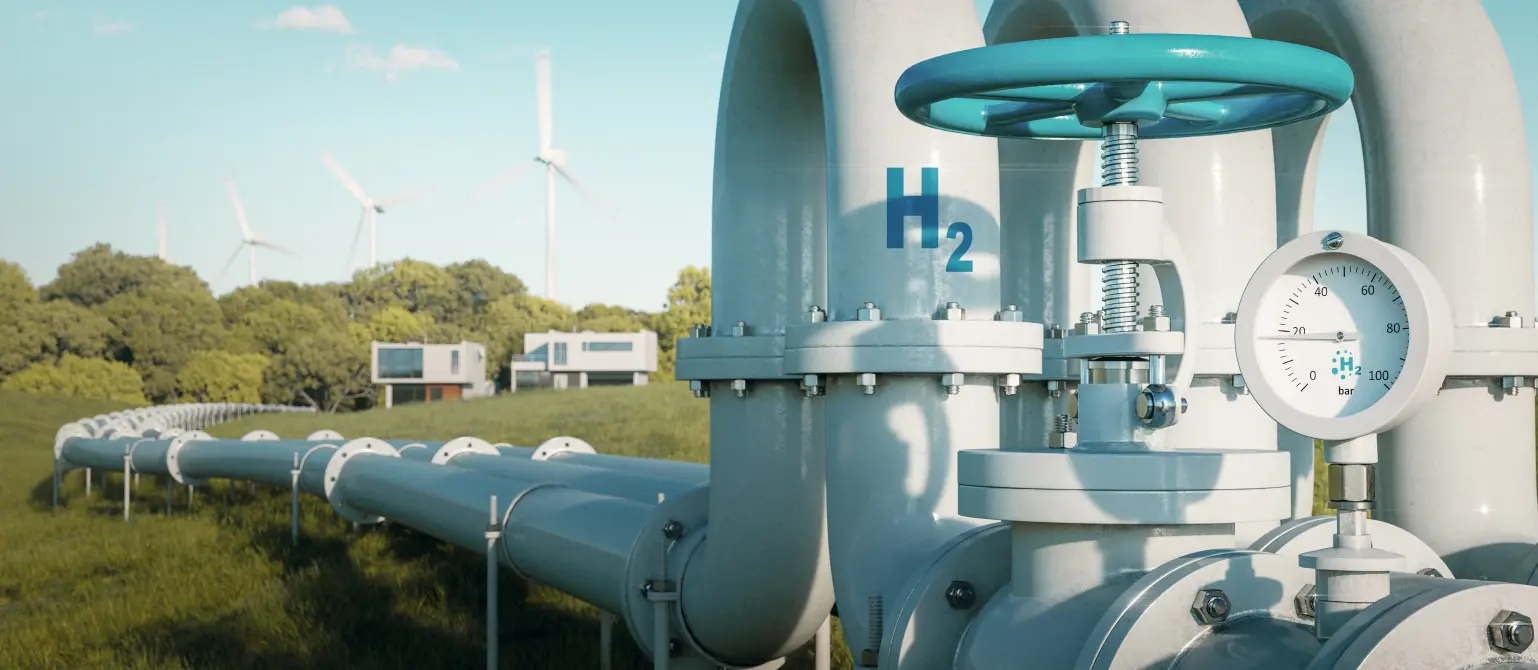 Eine Wasserstoffpipeline führt über eine grüne Wiese zu modernen Einfamilienhäusern. Im Hintergrund Windkraftanlagen.