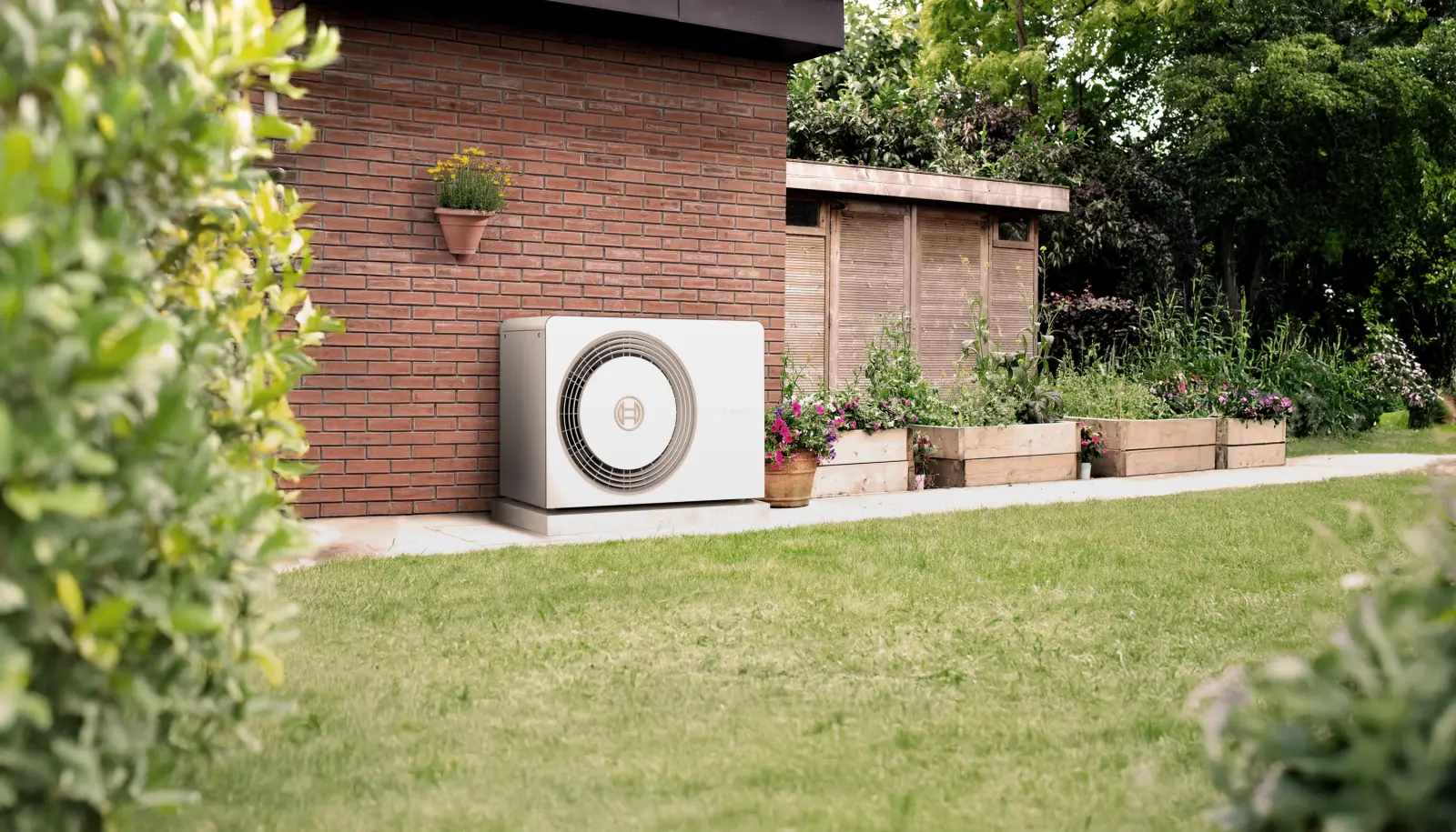 Eine Wärmepumpe steht im Garten vor einer Hauswand