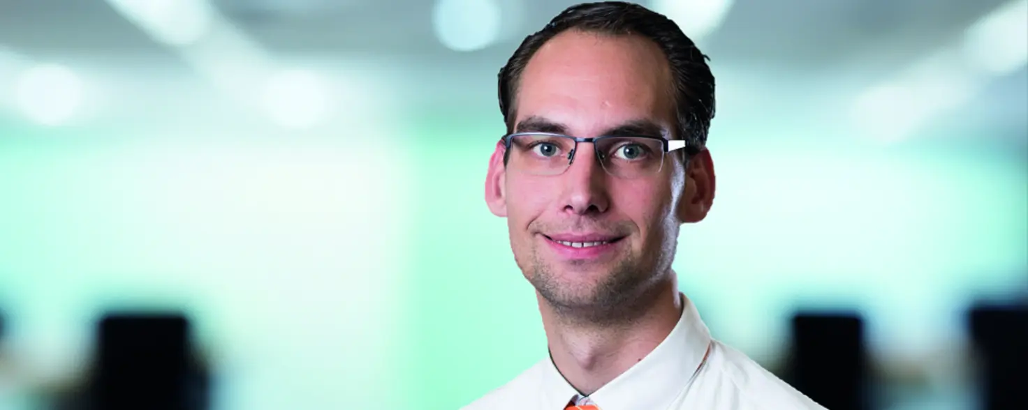 Porträtfoto: Tom Beier trägt ein weißes Hemd mit rotem Schlips und eine Brille.