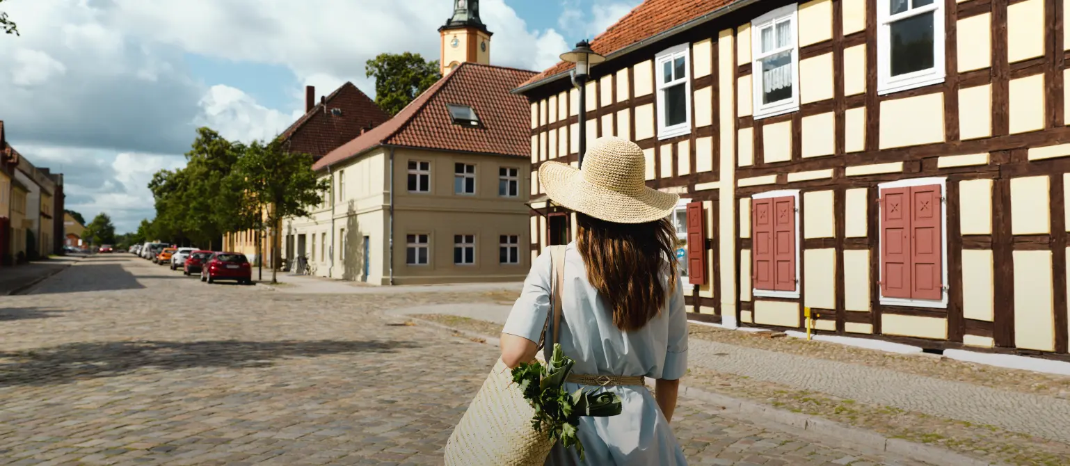 Eine Frau mit Sonnenhut ist von hinten zu sehen wie sie durch die Stadt läuft