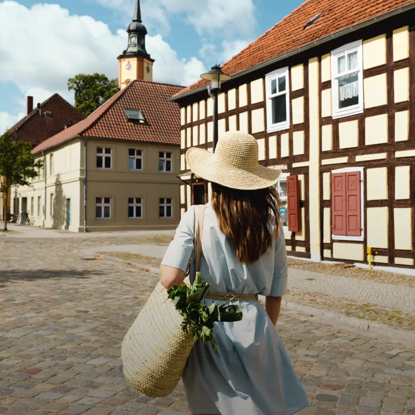 Eine Frau mit Sonnenhut ist von hinten zu sehen wie sie durch die Stadt läuft