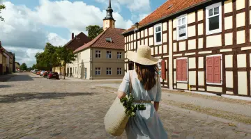 Eine Frau mit Sonnenhut ist von hinten zu sehen wie sie durch die Stadt läuft
