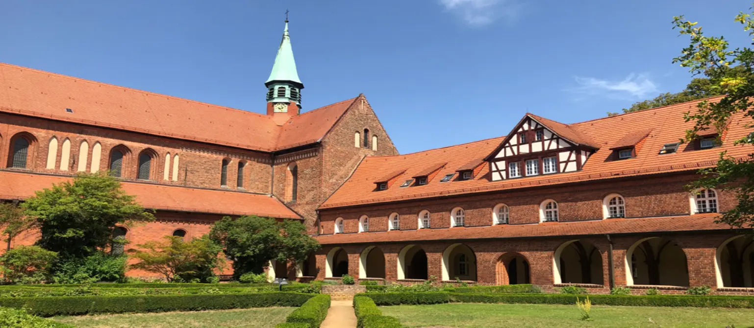 Ältestes Kloster in der Mark Brandenburg: rote Backsteingebäude des Klosters Lehnin mit Garten und blauem Himmel.