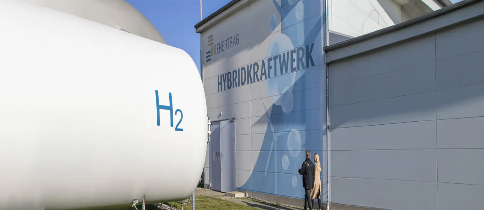 Ein Wasserstoff-Behälter vor einer silbergrauen Industriehalle mit der Aufschrift 